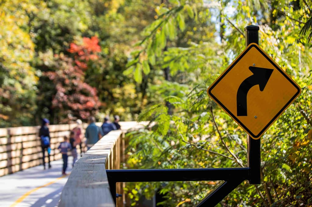 People walking on the Bob Callan trail with close-up of a sign indicating a right turn