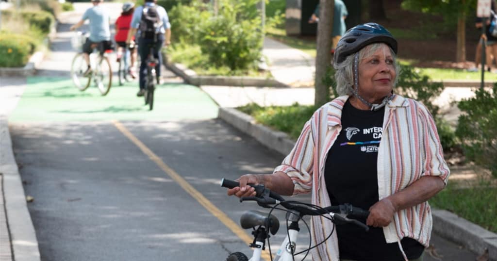 An older adult standing with her bicycle on a greenway trail